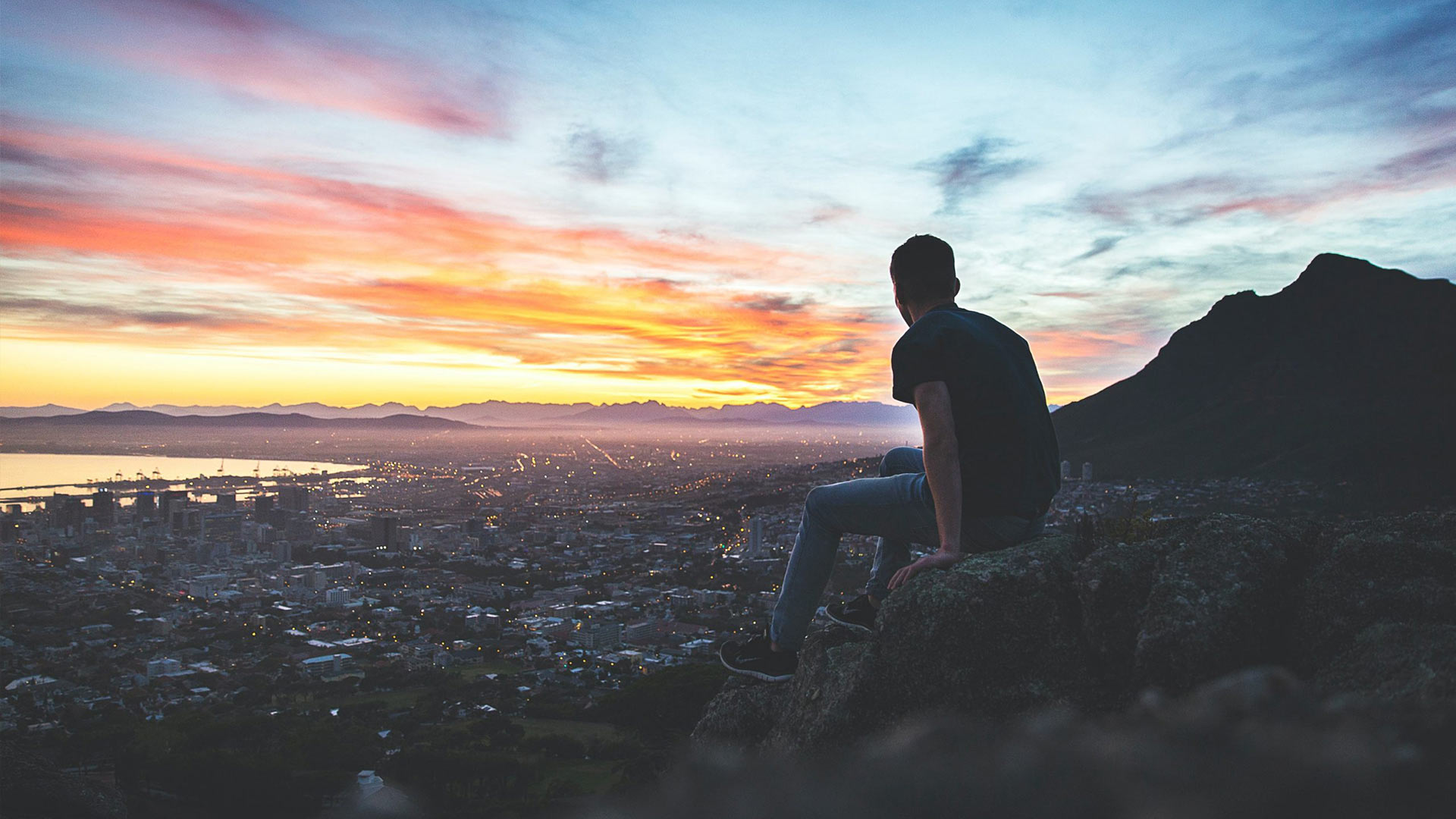 A man sitting on a hill overlooking a city